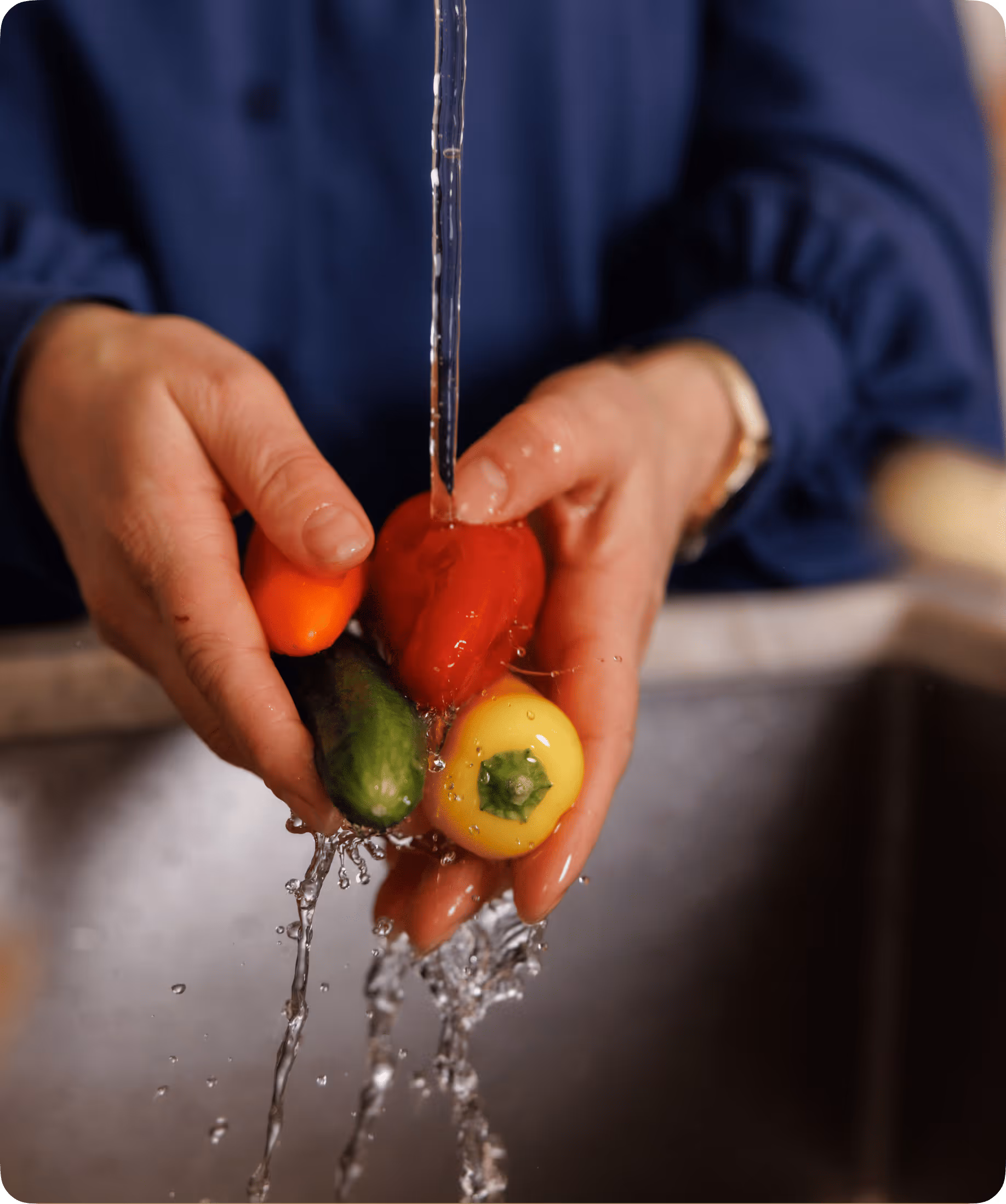 Handen die kleurrijke minipaprika’s onder stromend water in een gootsteen wassen.