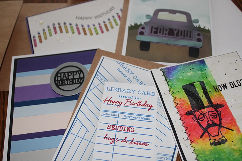 Various colorful birthday cards including designs with candles, a car, library card motif, and a rainbow background with a drawing of a man in a top hat.