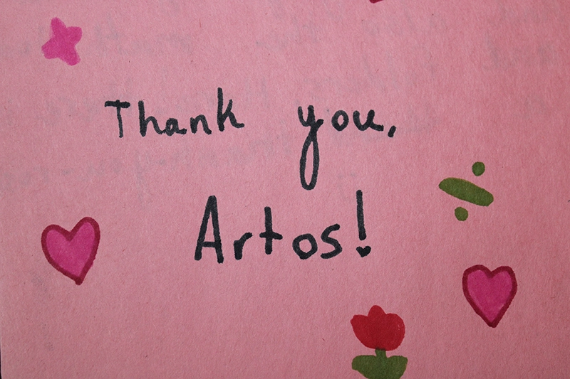Child's pink thank you card decorated with hand-drawn flowers, hearts, a sun, and handwritten messages saying 'Thank You So Much' and 'Thank you for the things you gave us.' An Artos appreciation note.
