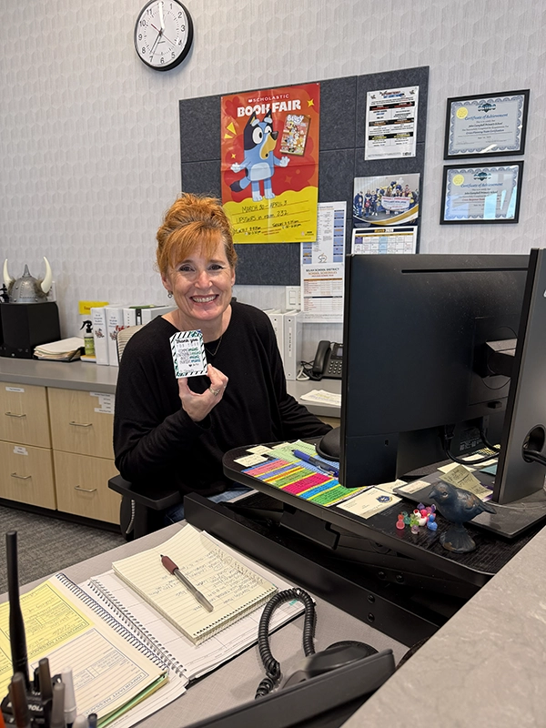 Smiling woman sitting at her desk in an office holding a small patterned card.