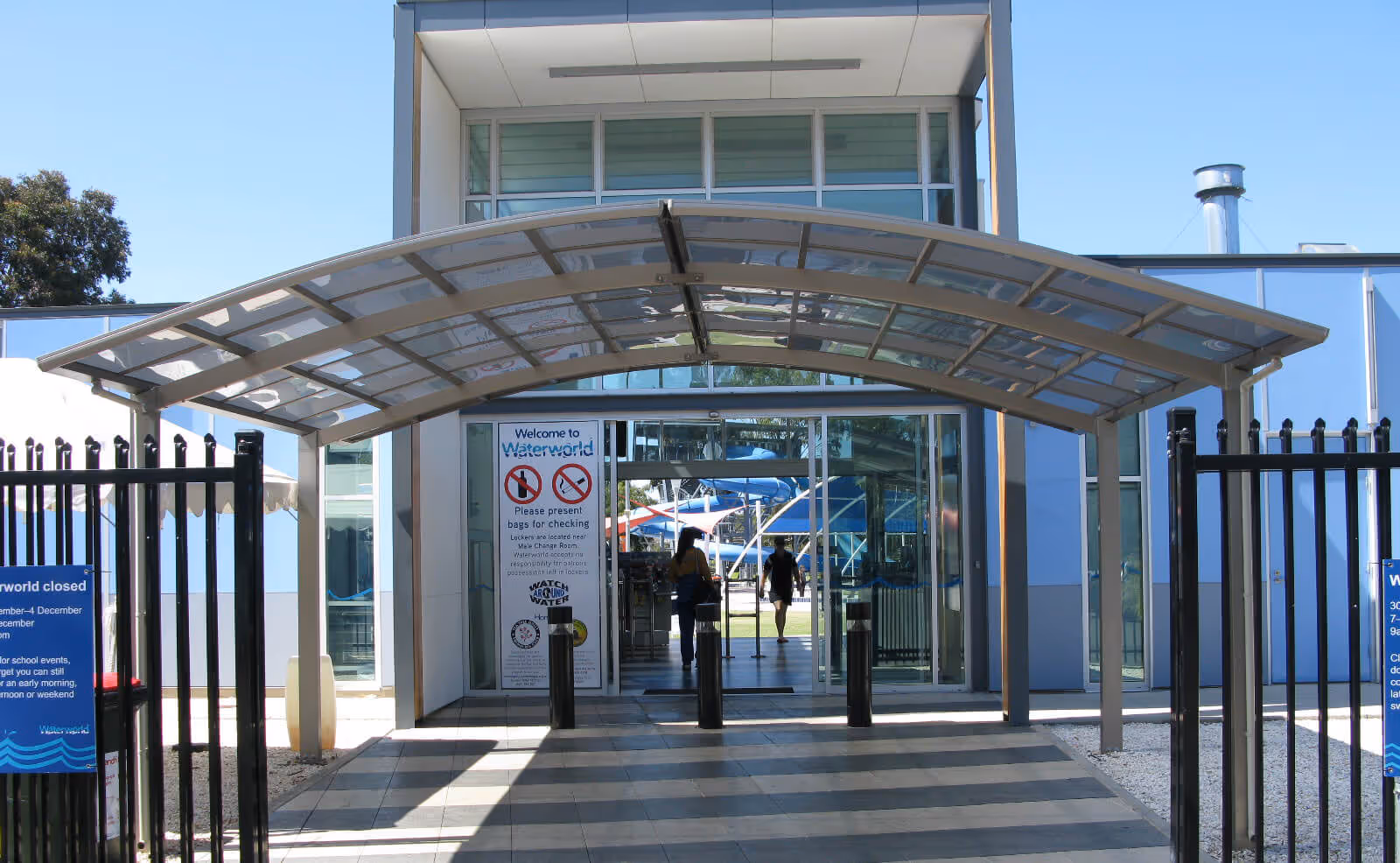 Entrance to Waterworld with a curved glass canopy, black metal gates, and visible water slides inside.