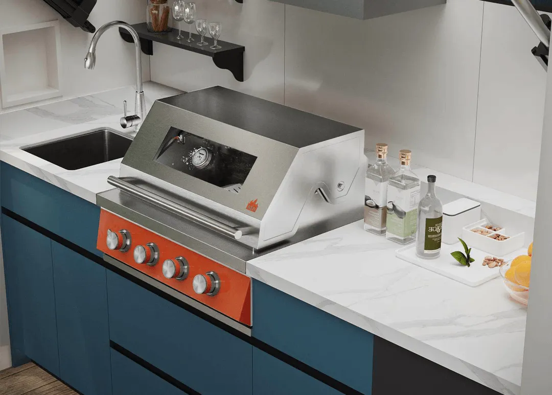 Modern kitchen countertop with a stainless steel grill featuring five control knobs and a built-in thermometer, next to a sink and bottles on the counter.