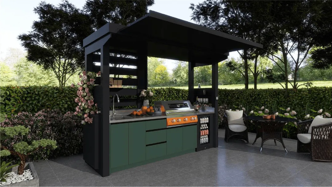 Outdoor kitchen setup with black and green cabinetry, an orange grill, sink, and countertop adorned with pumpkins and flowers, next to a seating area with wicker chairs and a table surrounded by greenery.