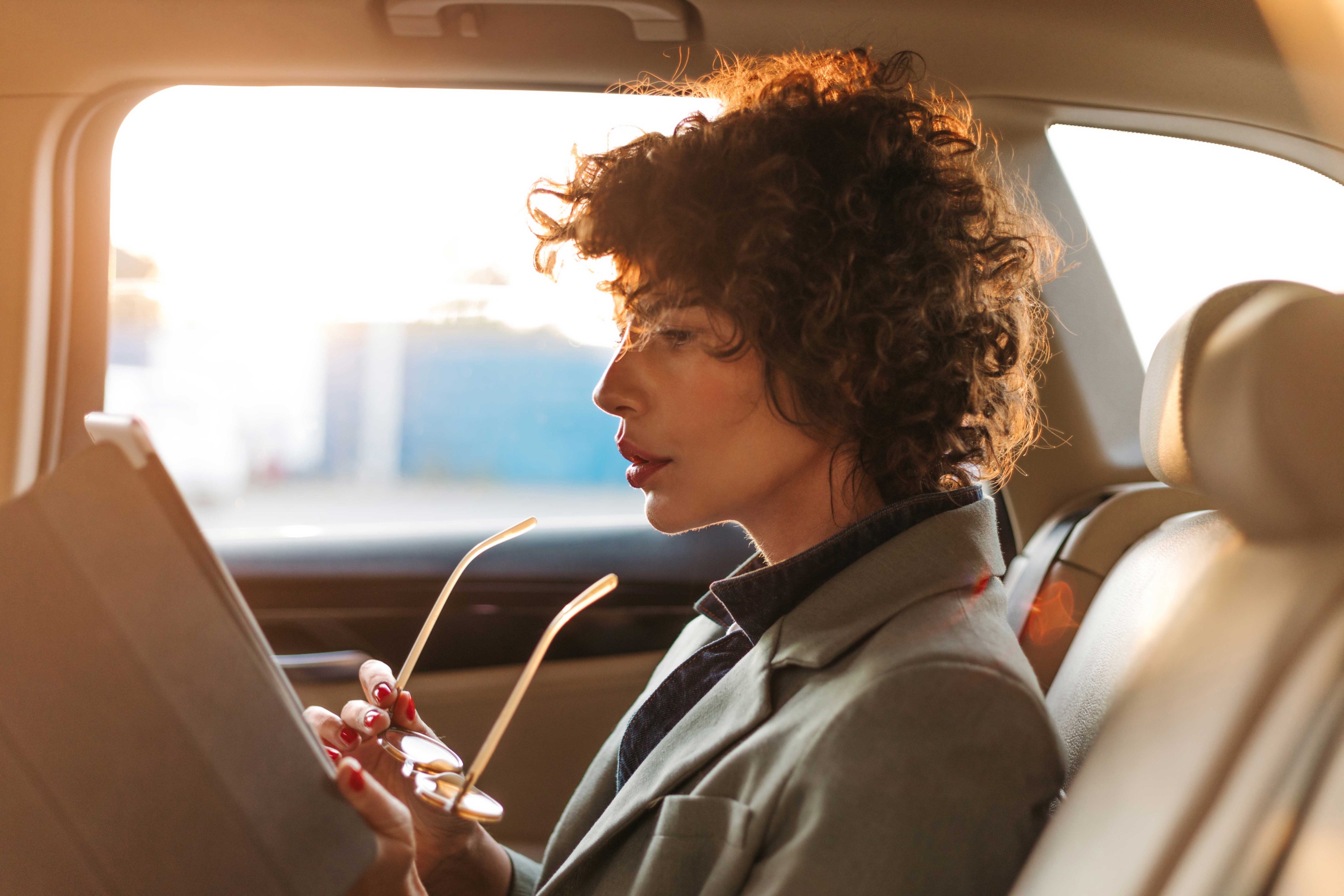 Executive woman reviewing document on a tablet in the rear seat of a luxury vehicle
