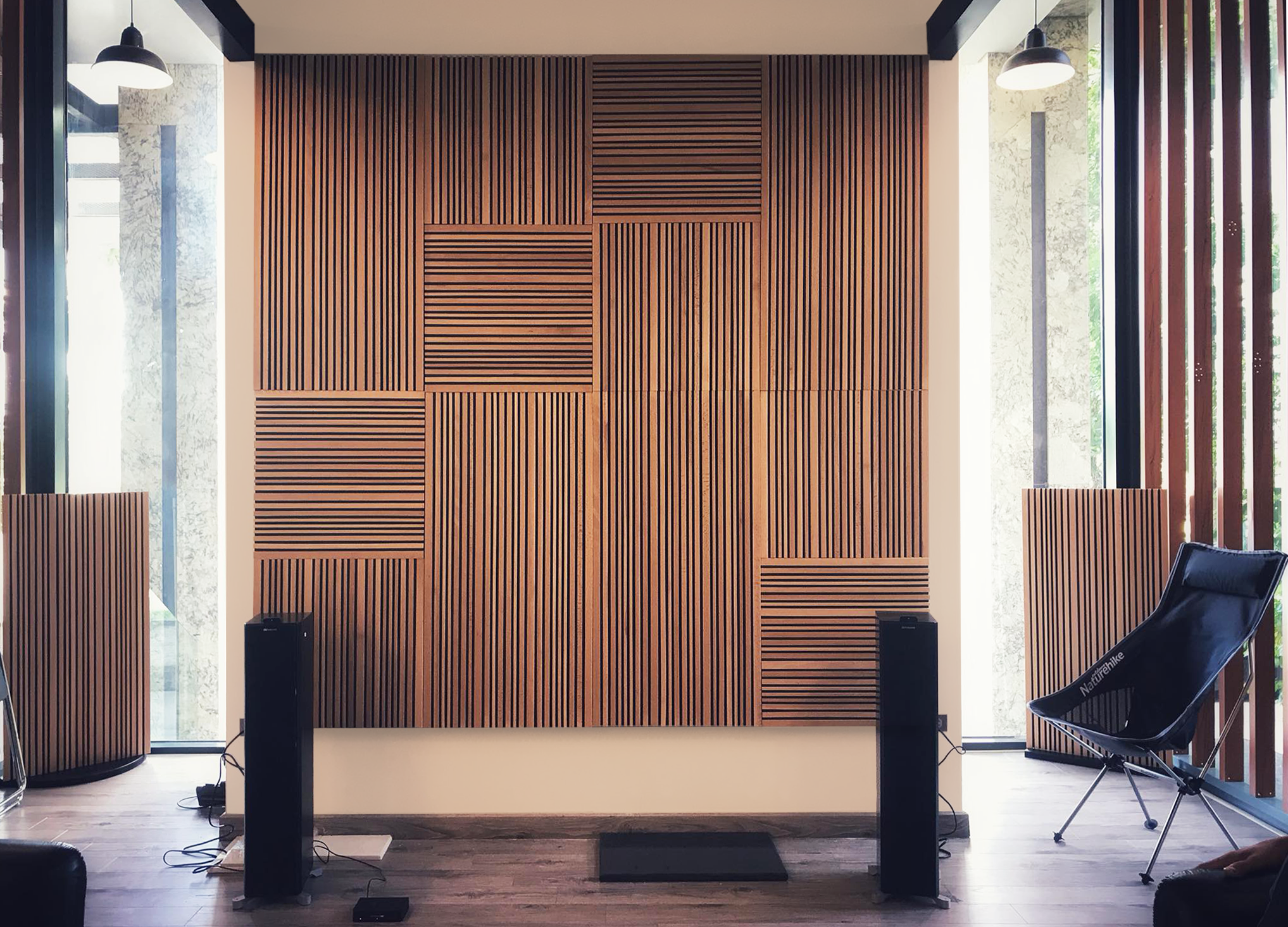 Modern room with wooden acoustic panels, two black speakers, and a black folding chair by a large window.