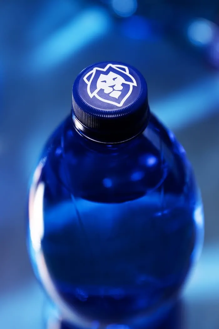 Detail modrého uzávěru láhve s vodou s bílým logem lva na vrcholu.