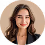 Smiling woman with long dark hair wearing a brown blazer over a dark top, against a white background.