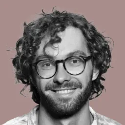 A man with curly hair wearing glasses and a white shirt.