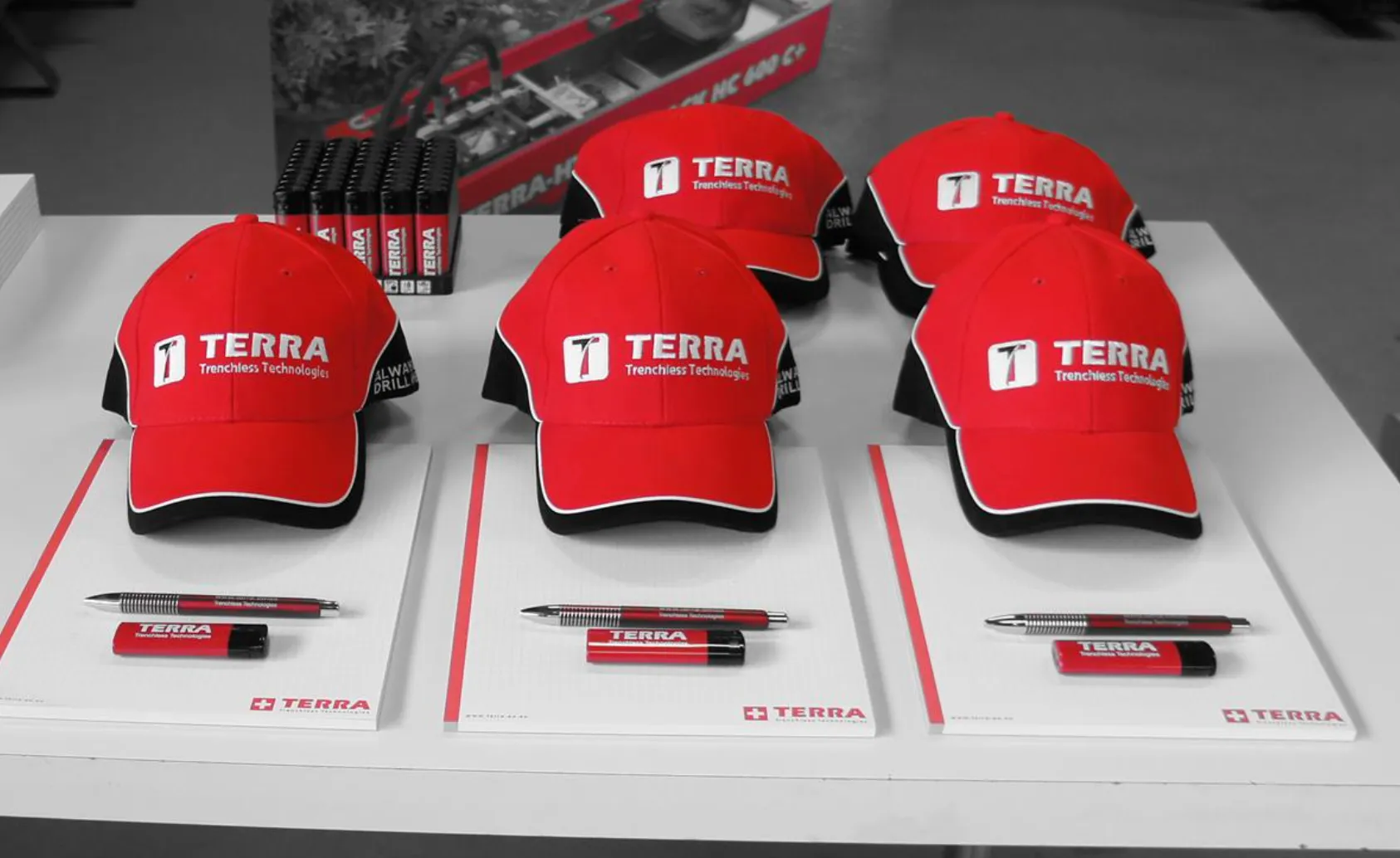 Trois capuchons TERRA rouges, chacun disposé sur une table avec un stylo, une clé USB et un bloc-notes.