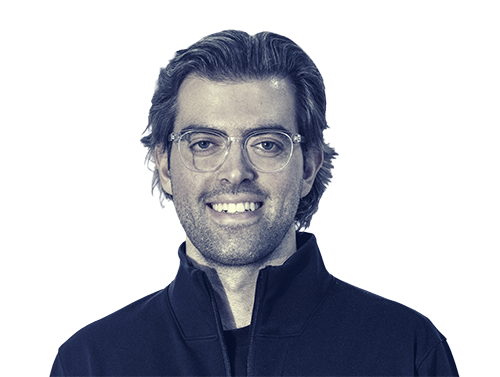 Smiling man with glasses and dark jacket facing forward on a white background.
