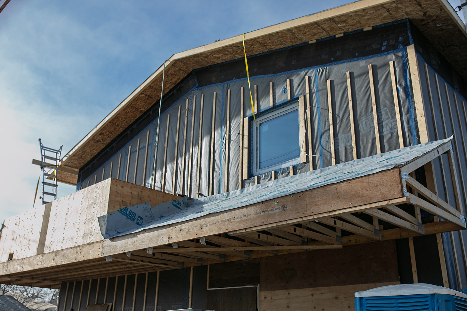 Partially constructed house with exposed wooden framing and a blue portable toilet nearby.