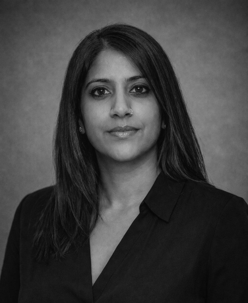 Black and white portrait of a woman with long straight hair wearing a dark blouse, looking directly at the camera.
