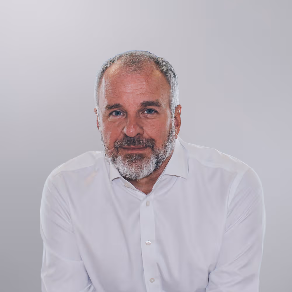 Middle-aged man with gray beard and short hair wearing a white button-up shirt against a gray background.