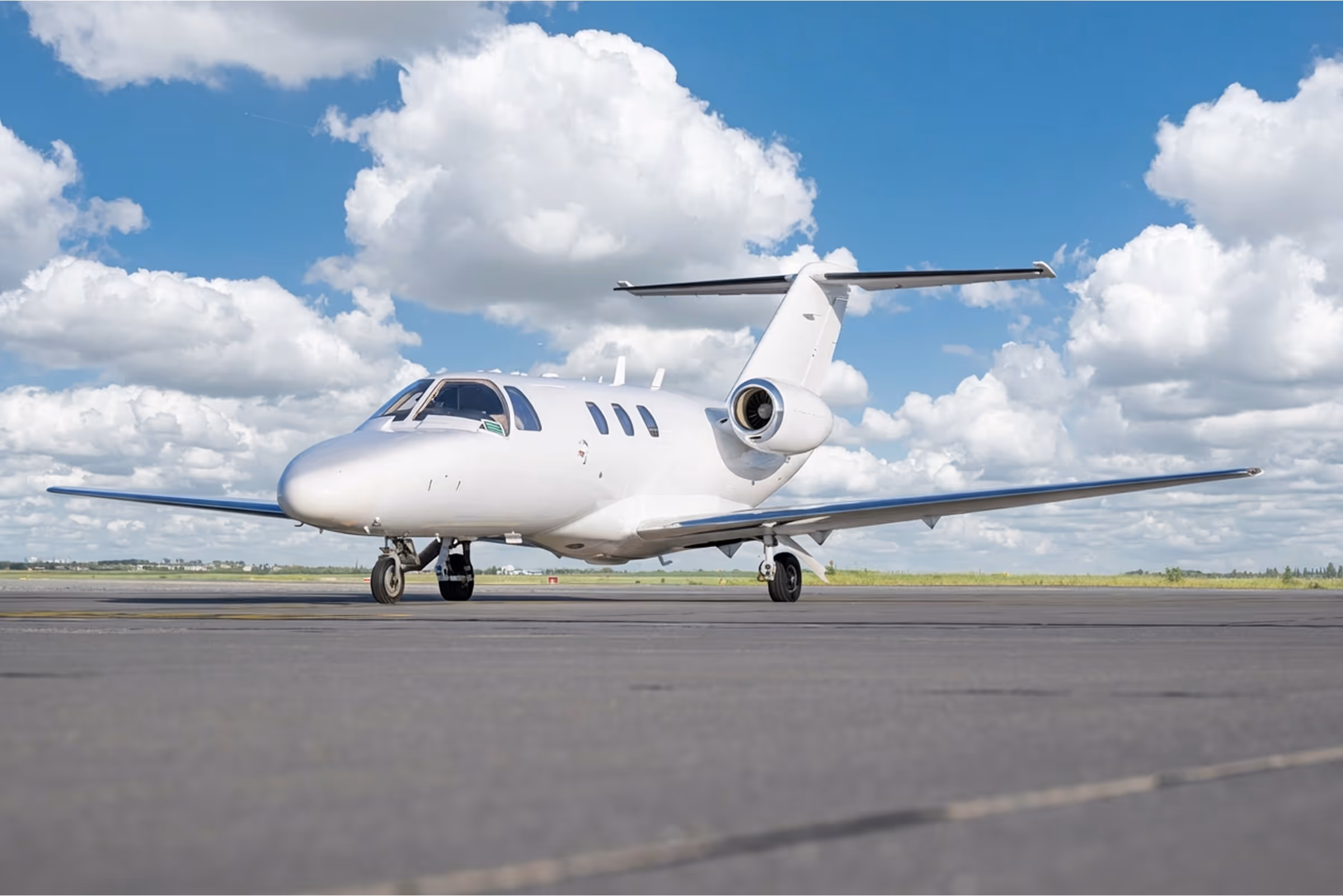 White private jet parked on runway under a partly cloudy blue sky.