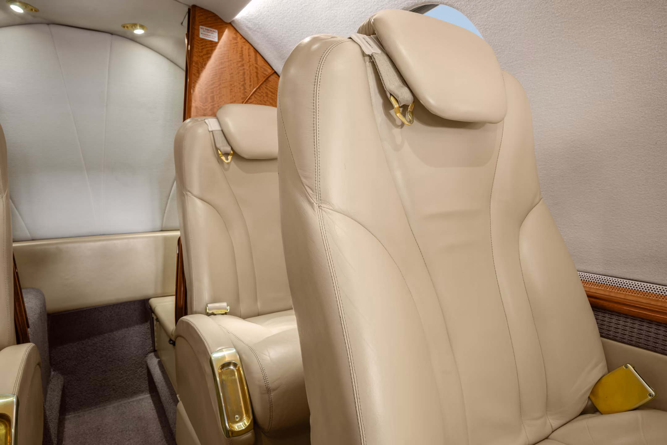 Interior view of a private jet with a gray leather seat, a padded bench, wall hooks holding two face masks, and small storage compartments.