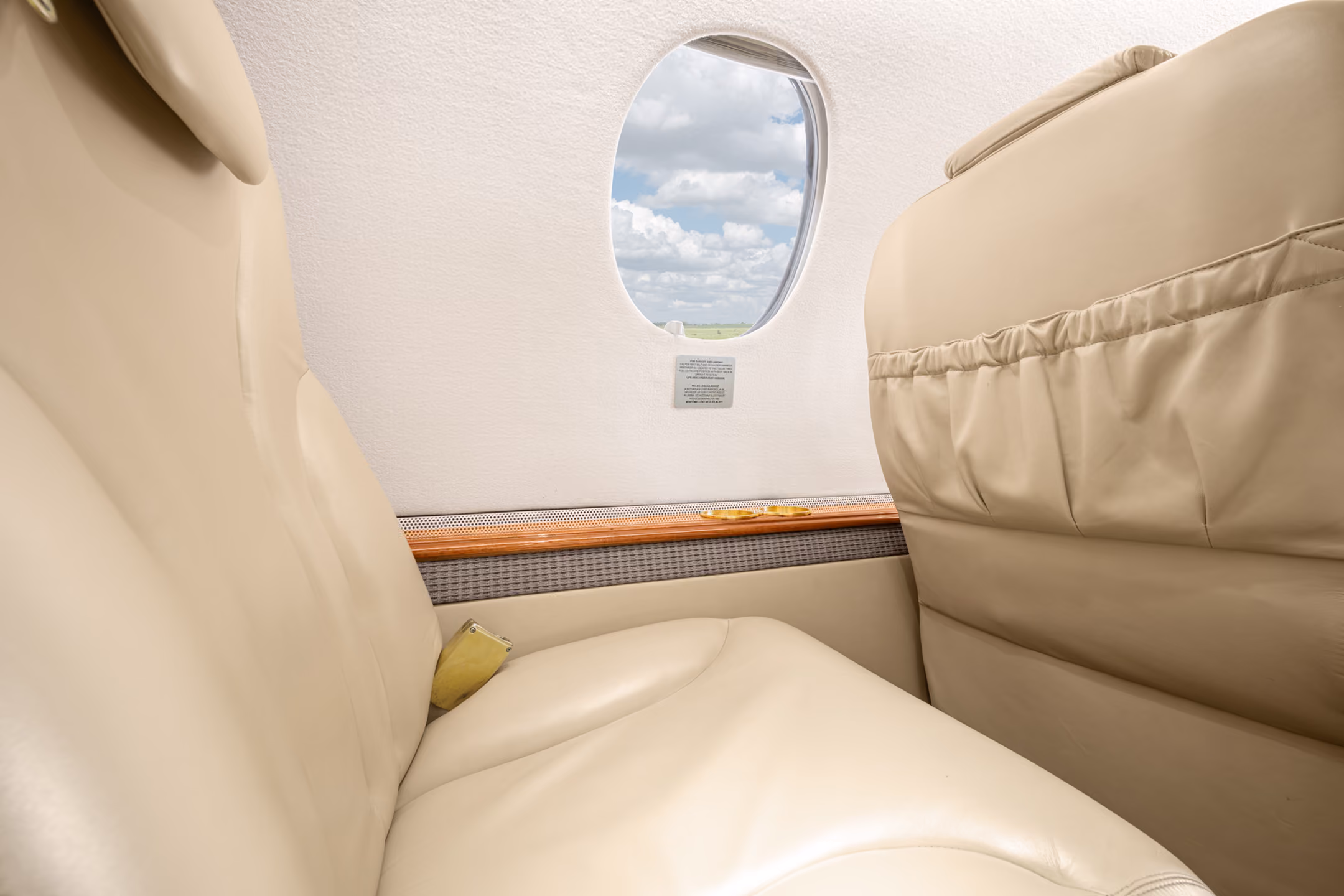 Interior of a small private jet with two facing gray leather seats and four windows showing a blue sky.