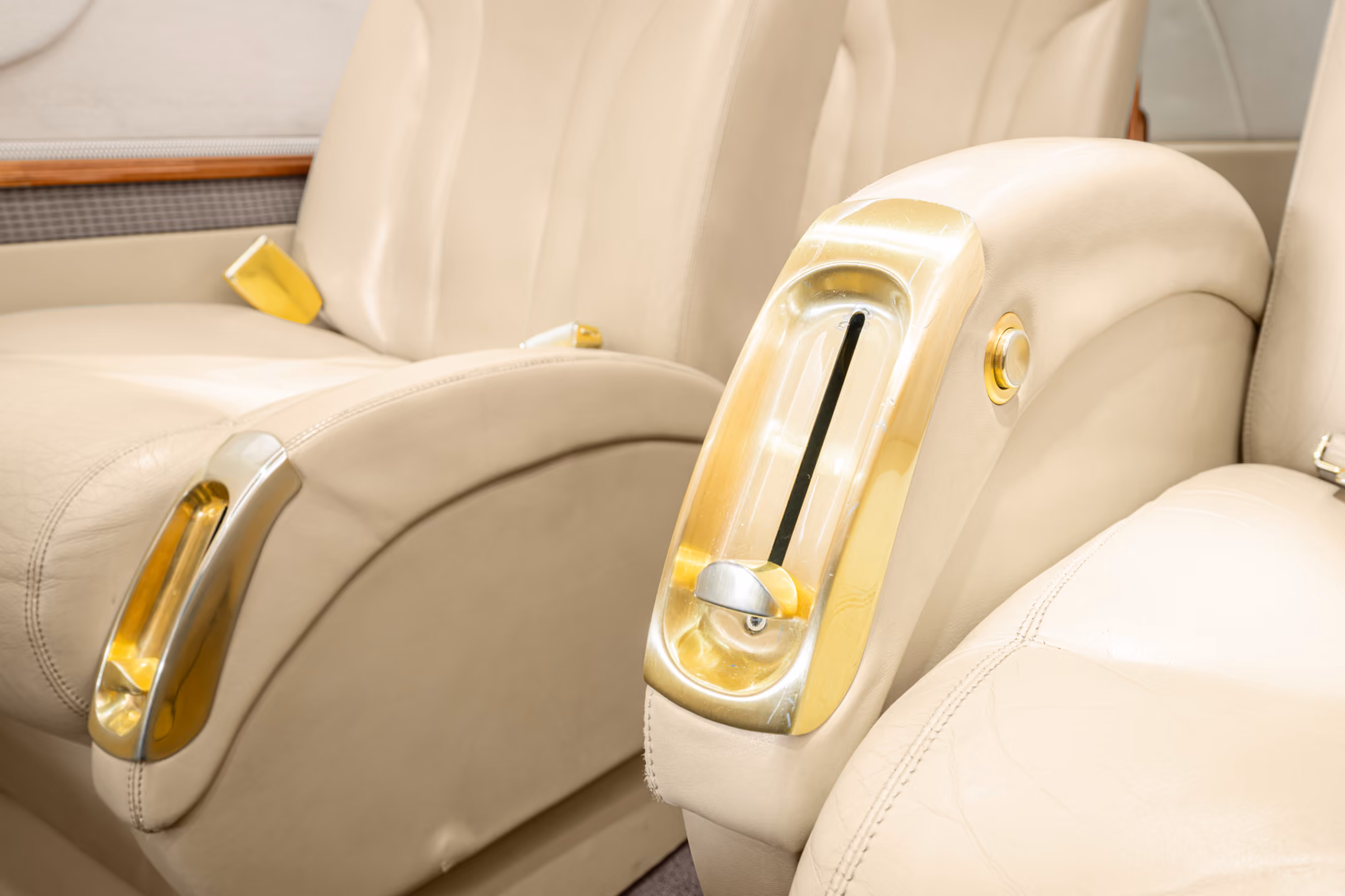 Interior view of a private jet with a gray leather seat, a padded bench, wall hooks holding two face masks, and small storage compartments.
