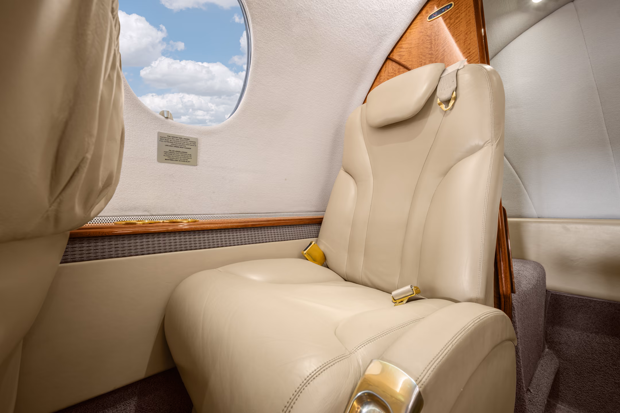 Interior view of a private jet cabin showing two gray leather seats facing each other with a fold-out table and four windows.