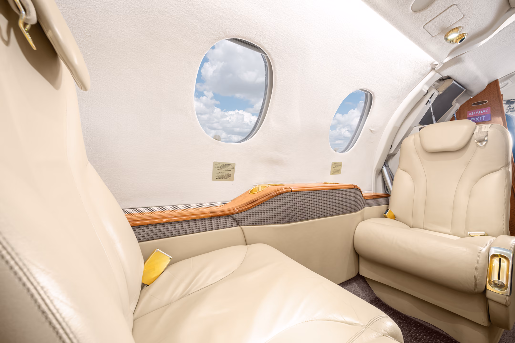Gray leather passenger seat inside a private jet cabin next to two windows with blue sky outside.