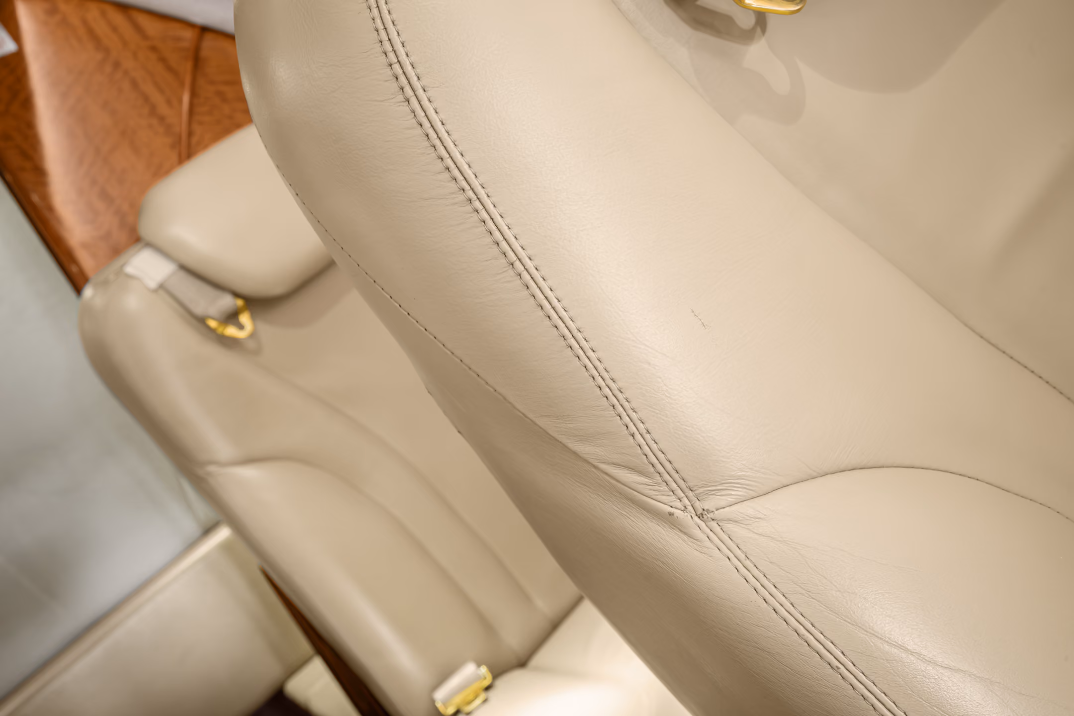 Interior view of a private jet with a gray leather seat, a padded bench, wall hooks holding two face masks, and small storage compartments.
