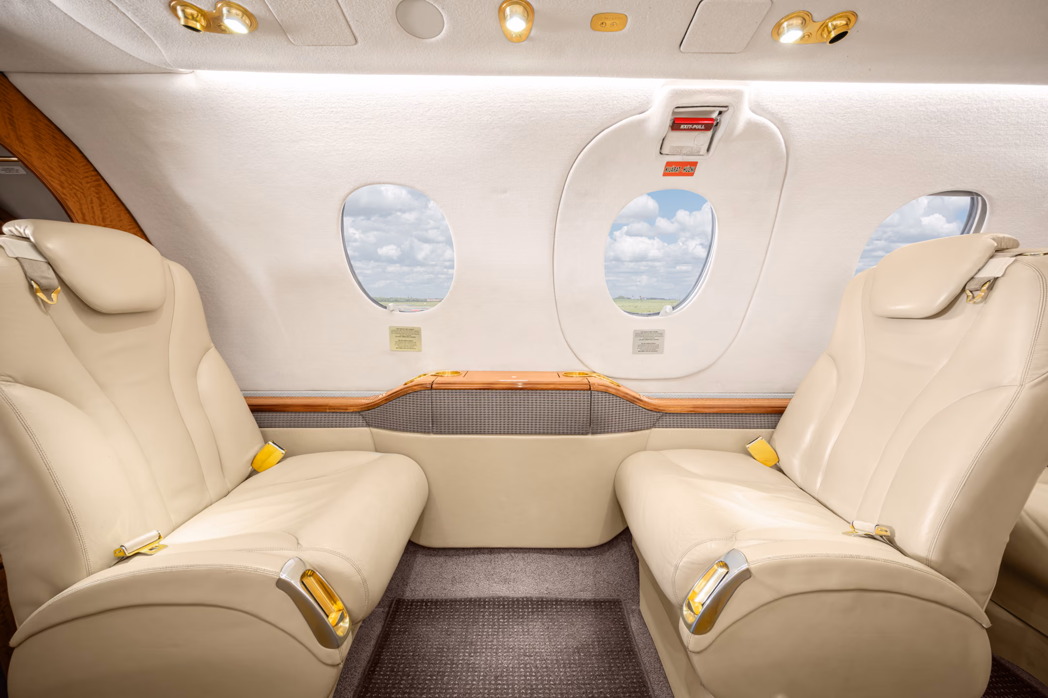 Interior view of a private jet with a gray leather seat, a padded bench, wall hooks holding two face masks, and small storage compartments.