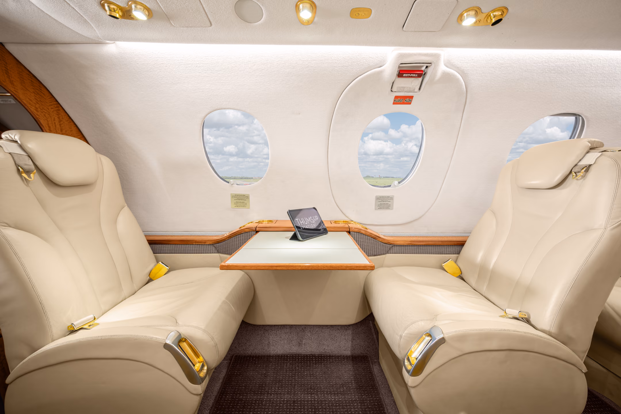 Interior view of a private jet with a gray leather seat, a padded bench, wall hooks holding two face masks, and small storage compartments.