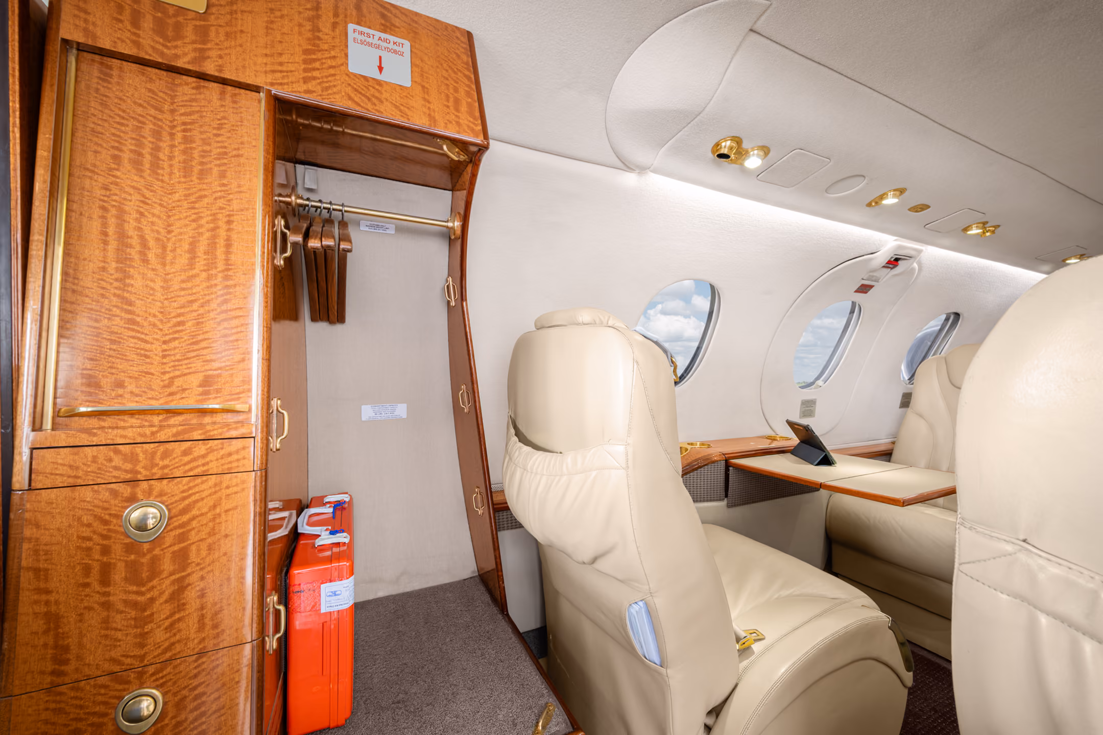 Interior of a private jet with gray leather seats and a storage cabinet holding a basket of snacks between the seats.