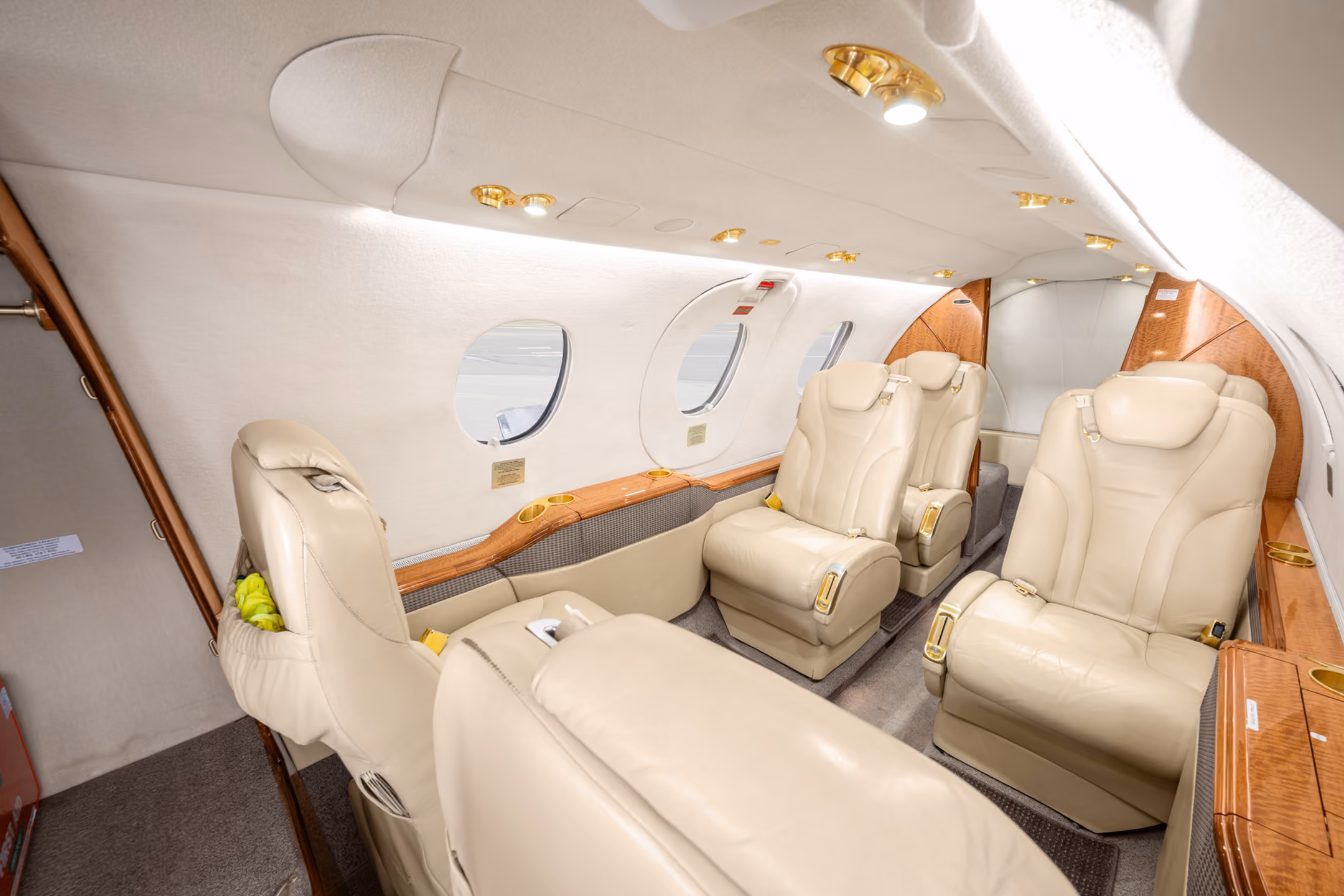 Interior view of a private jet with a gray leather seat, a padded bench, wall hooks holding two face masks, and small storage compartments.