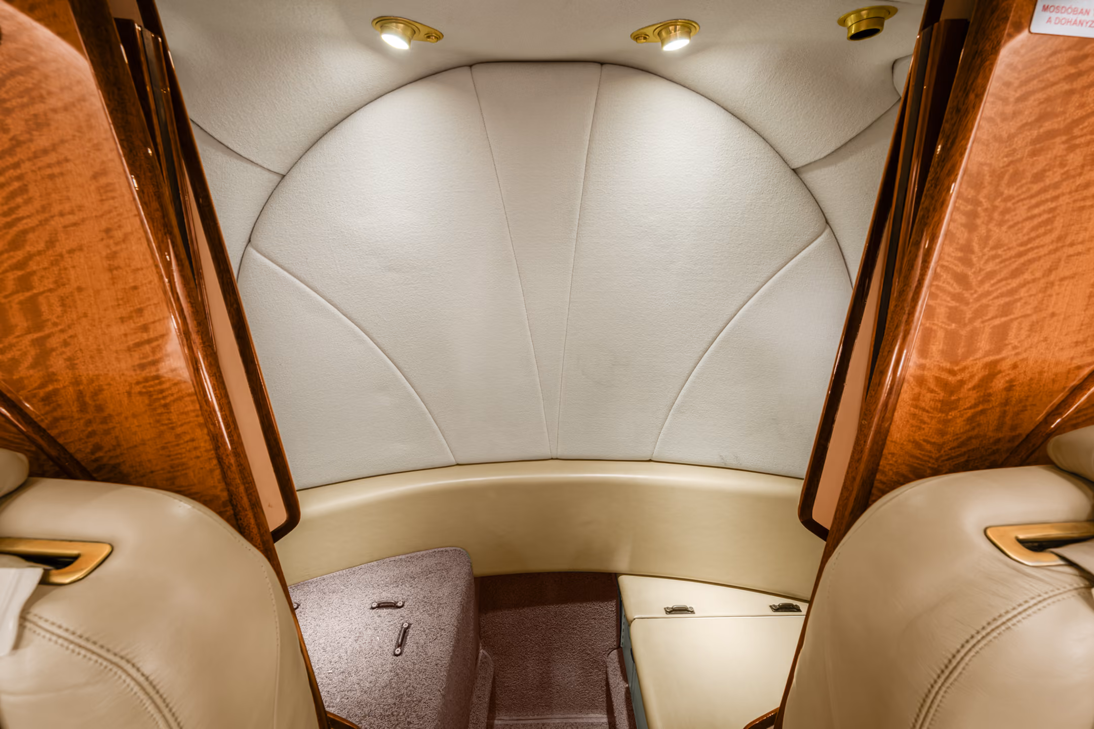 Interior of a small private jet with four gray leather seats, two on each side facing each other, and oval windows showing blue sky.