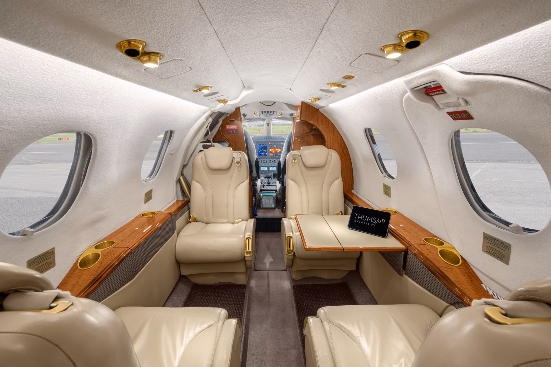 Interior of a private jet with gray leather seats arranged facing each other and a basket of assorted snacks near a window.
