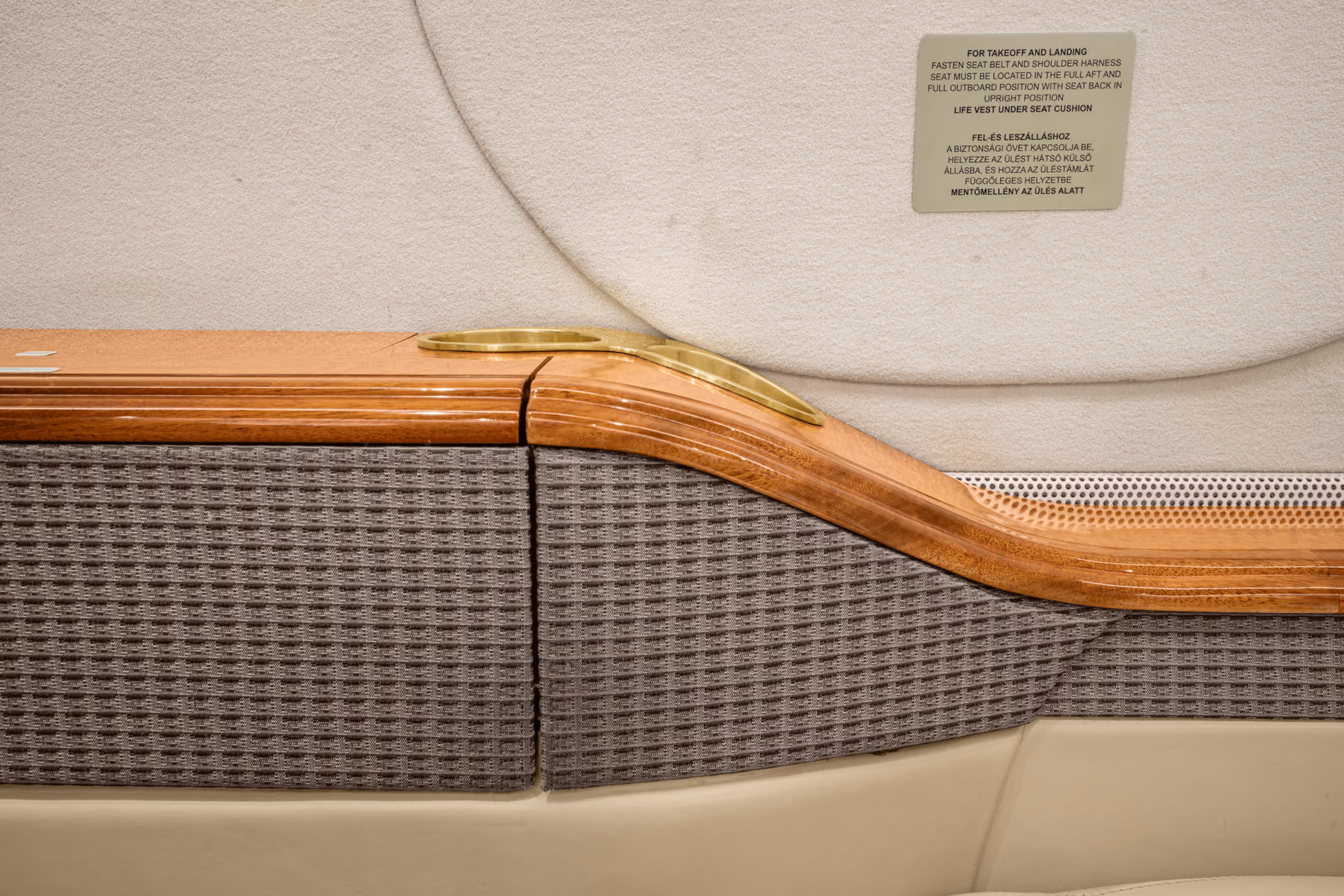 Interior view of a private jet with a gray leather seat, a padded bench, wall hooks holding two face masks, and small storage compartments.