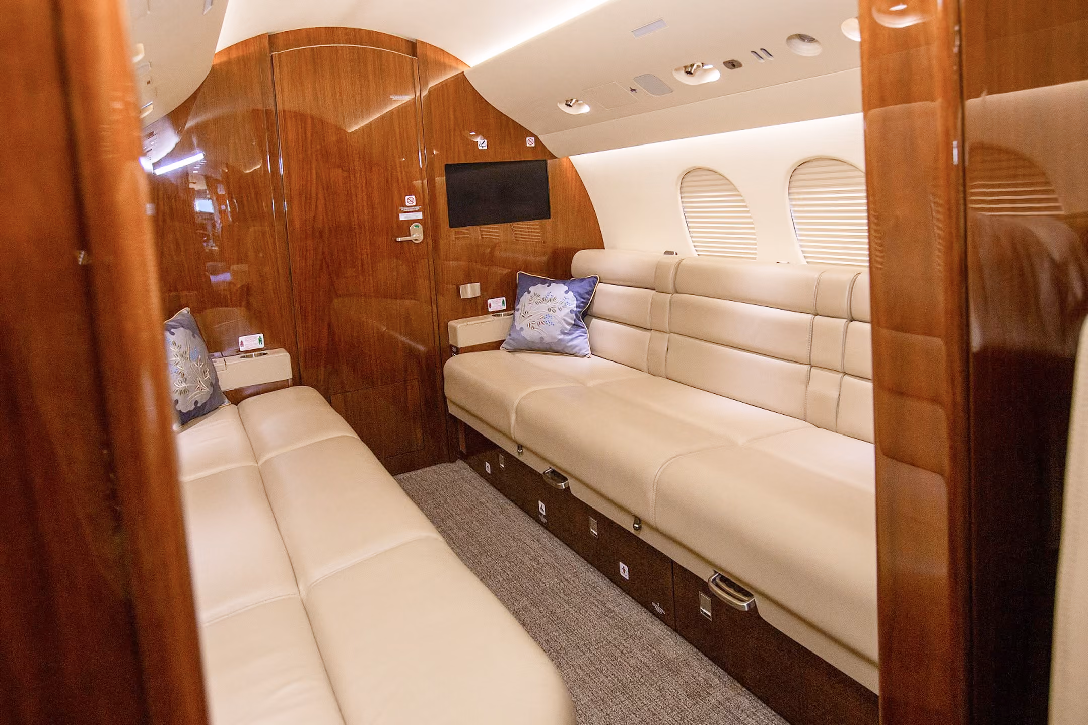 Interior of a private jet cabin with six gray leather seats arranged in pairs and windows on both sides.