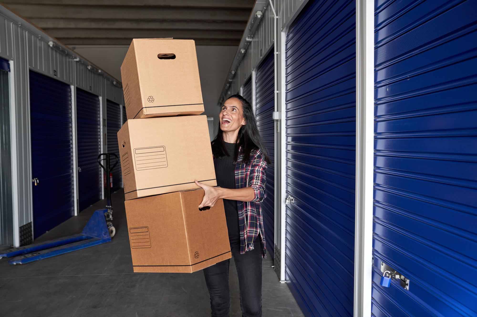 A woman carrying several boxes outside a self-storage unit