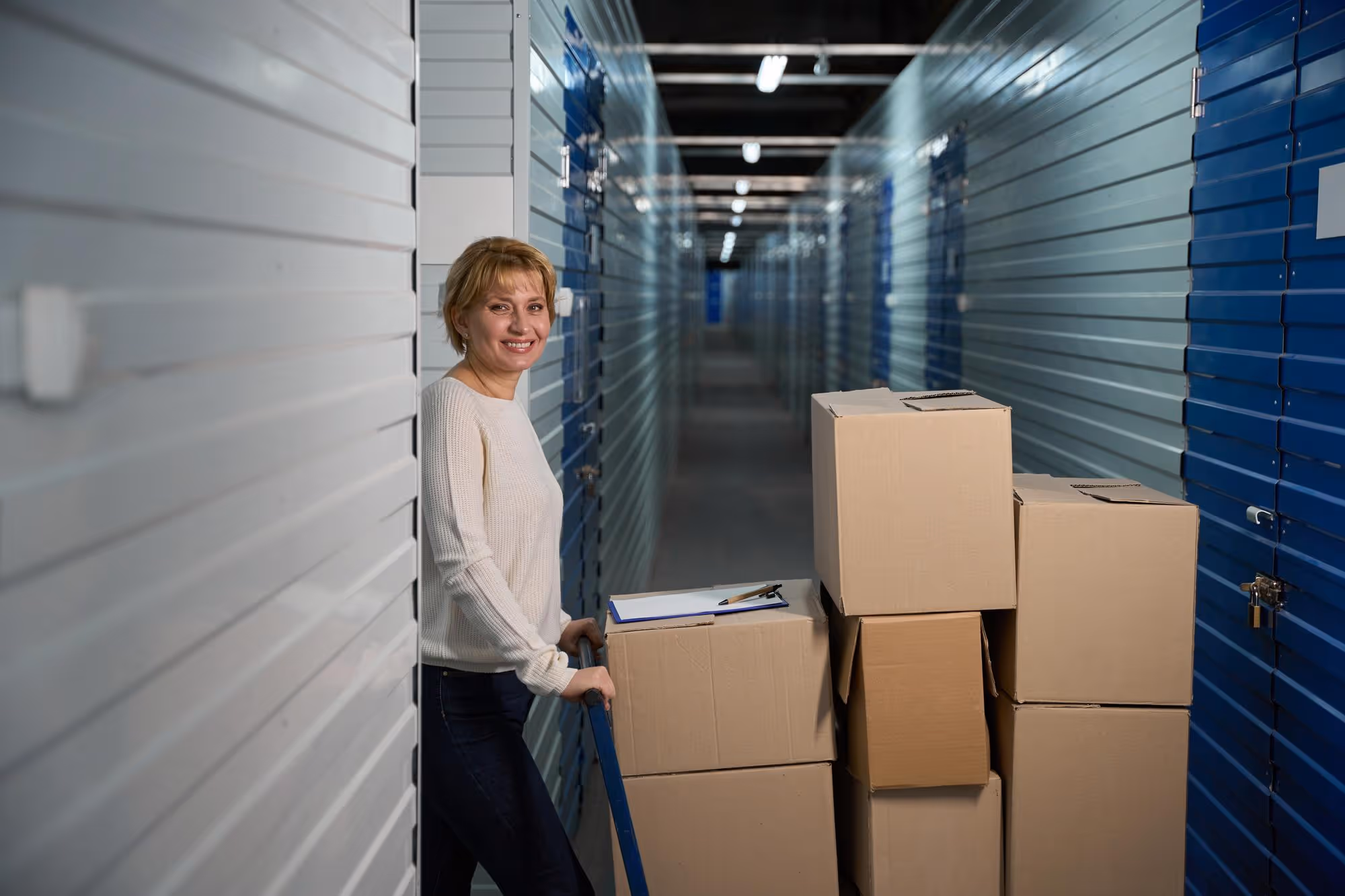 A woman wheeling a trolley loaded with boxes into a self-storage unit
