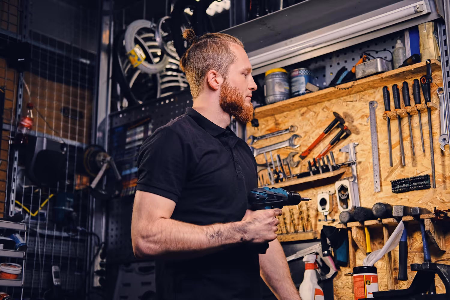 A man stood with an electric drill in front of a wall of various tools
