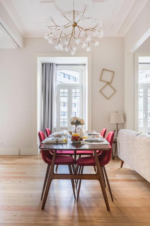 Dining table with red chairs set with plates and food beneath a modern chandelier in a bright room.