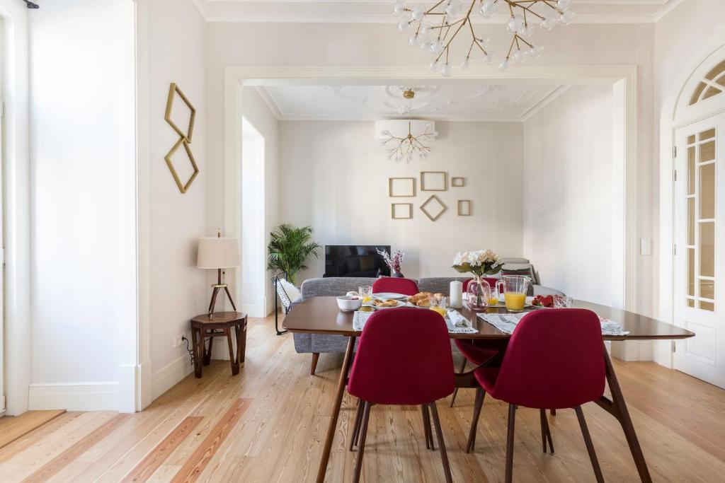 Modern dining room with red chairs, wooden table set for breakfast, and a gray sofa in the background.