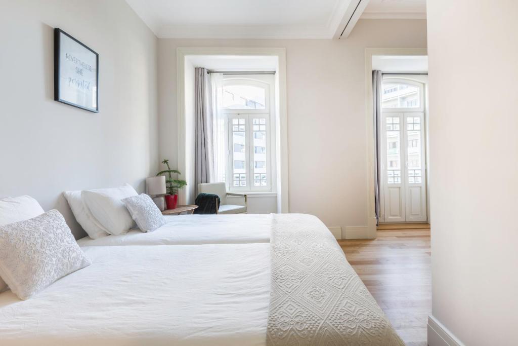 Bright bedroom with two white beds, pillows, a window, a chair, and a small plant on a nightstand.