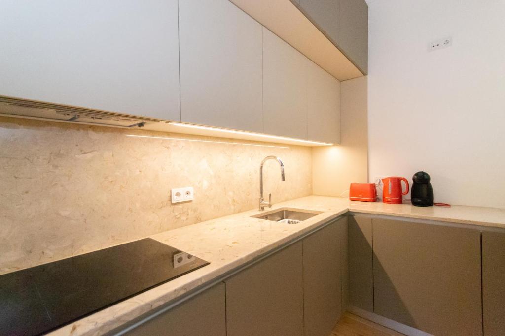 Modern kitchen corner with beige cabinets, marble countertop, sink, cooktop, and red appliances.