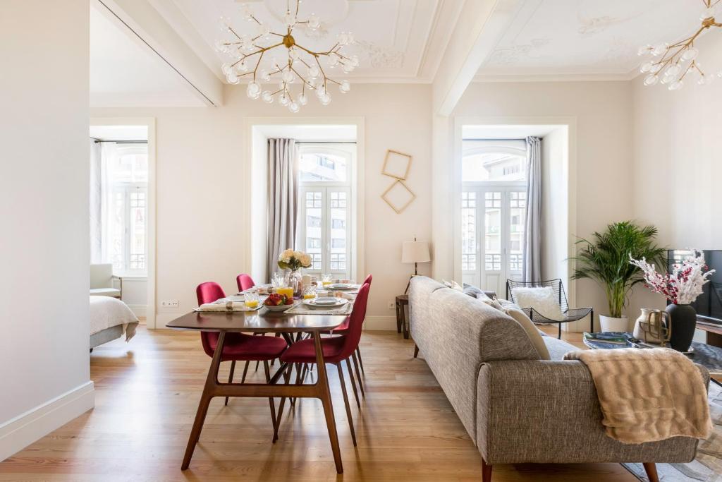 Bright modern living and dining area with wooden floors, red chairs, gray sofa, and large windows.