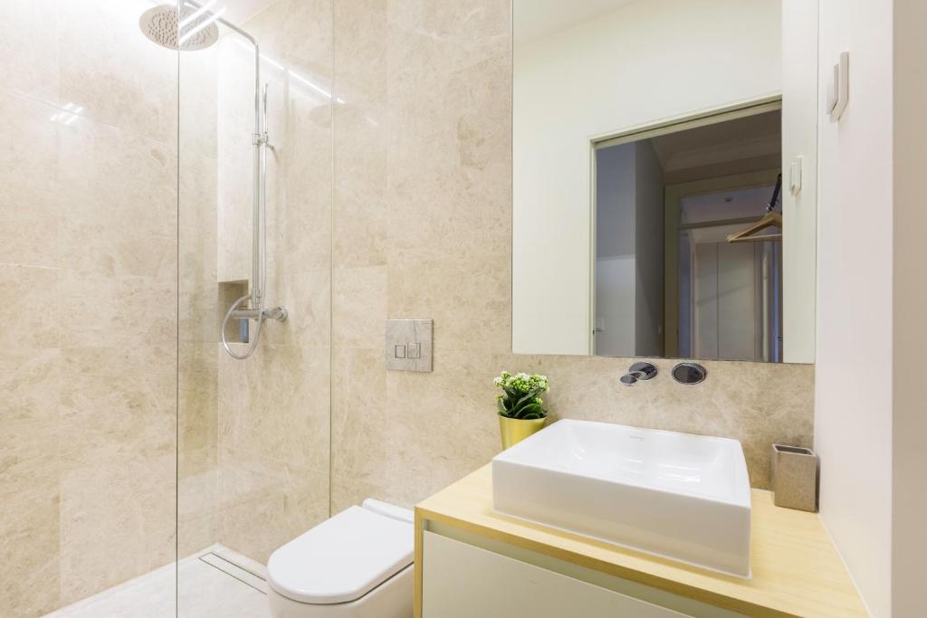 Modern bathroom with beige stone walls, glass shower, white toilet, and sink with mirror and plant.