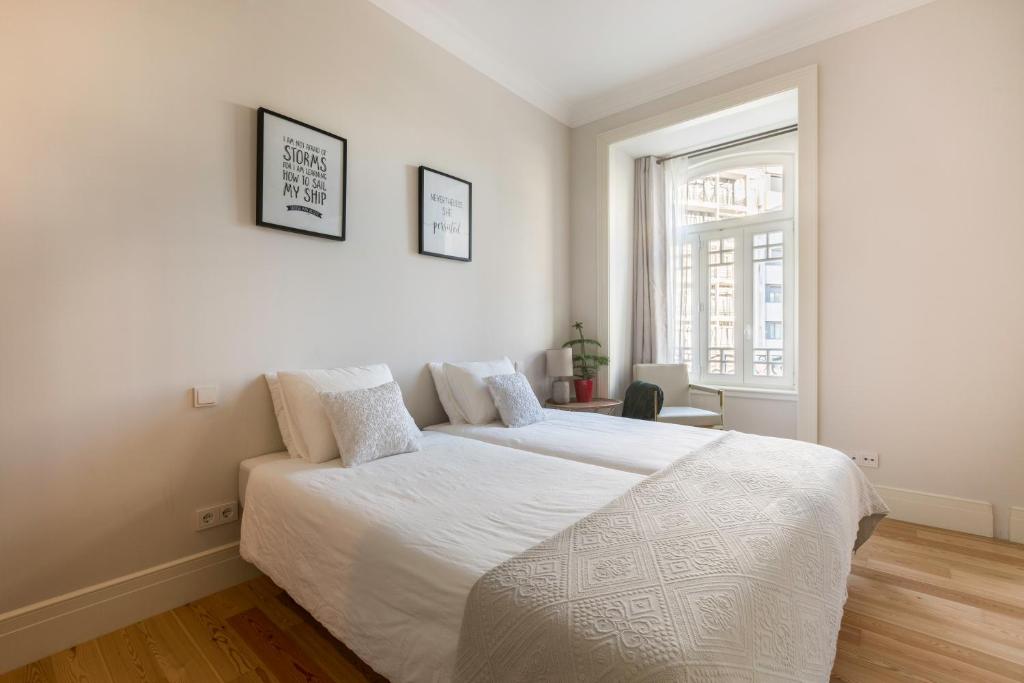 Minimalist bedroom with two twin beds, white linens, a chair by a large window, and framed quotes on the wall.
