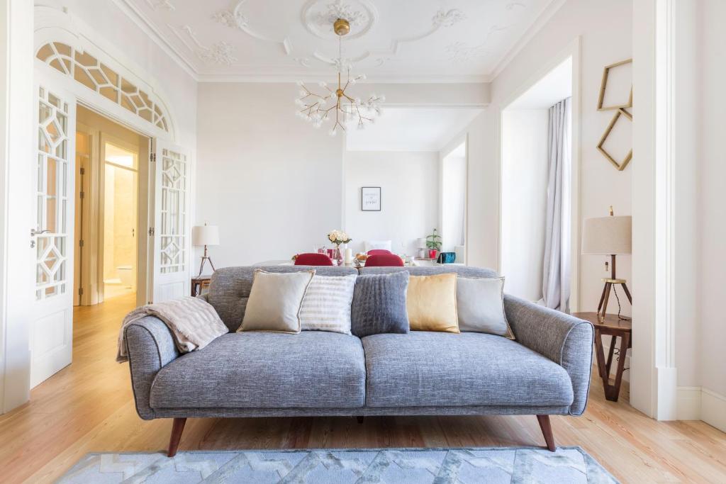 Modern living room with gray sofa, throw pillows, wooden floor, white walls, and chandelier.