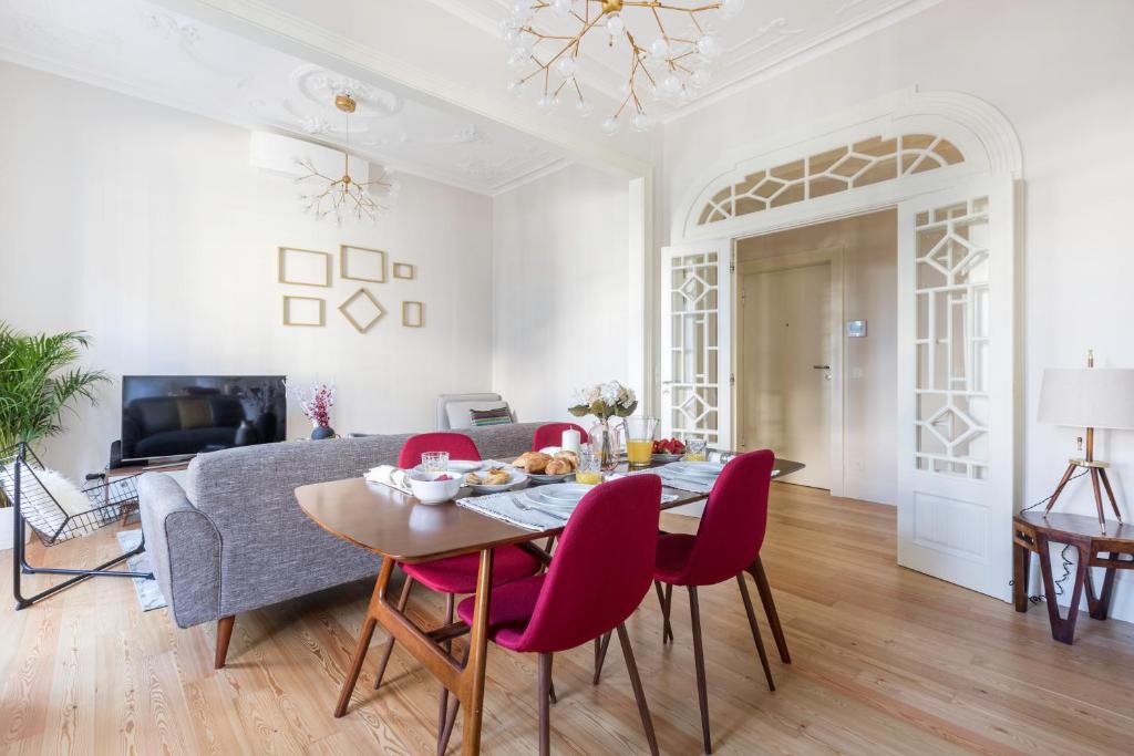 Dining table with red chairs set for breakfast in a bright living room with gray sofa and decorative white doors.