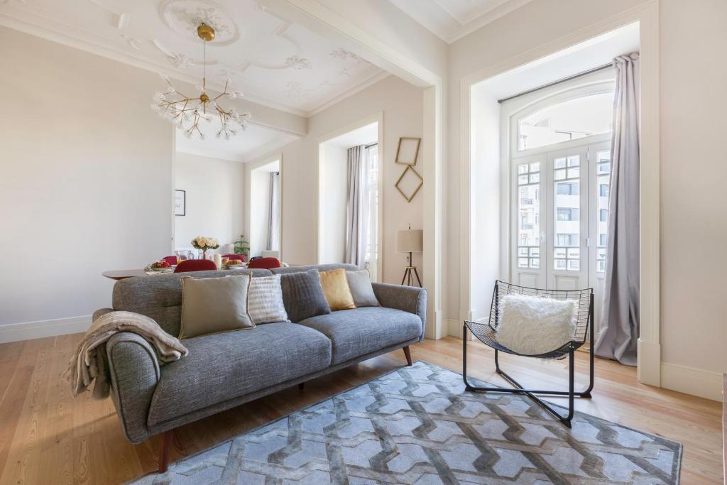 Bright living room with gray sofa, decorative pillows, modern chair, patterned rug, and large windows.