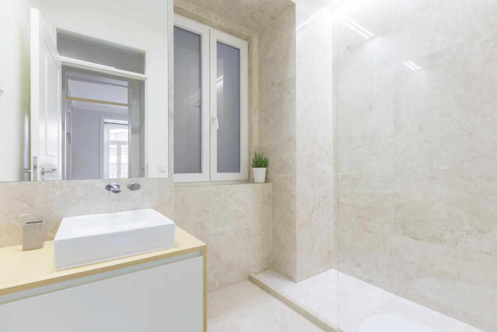 Minimalist bathroom with white sink, beige tiles, glass shower, and a small potted plant by the window.