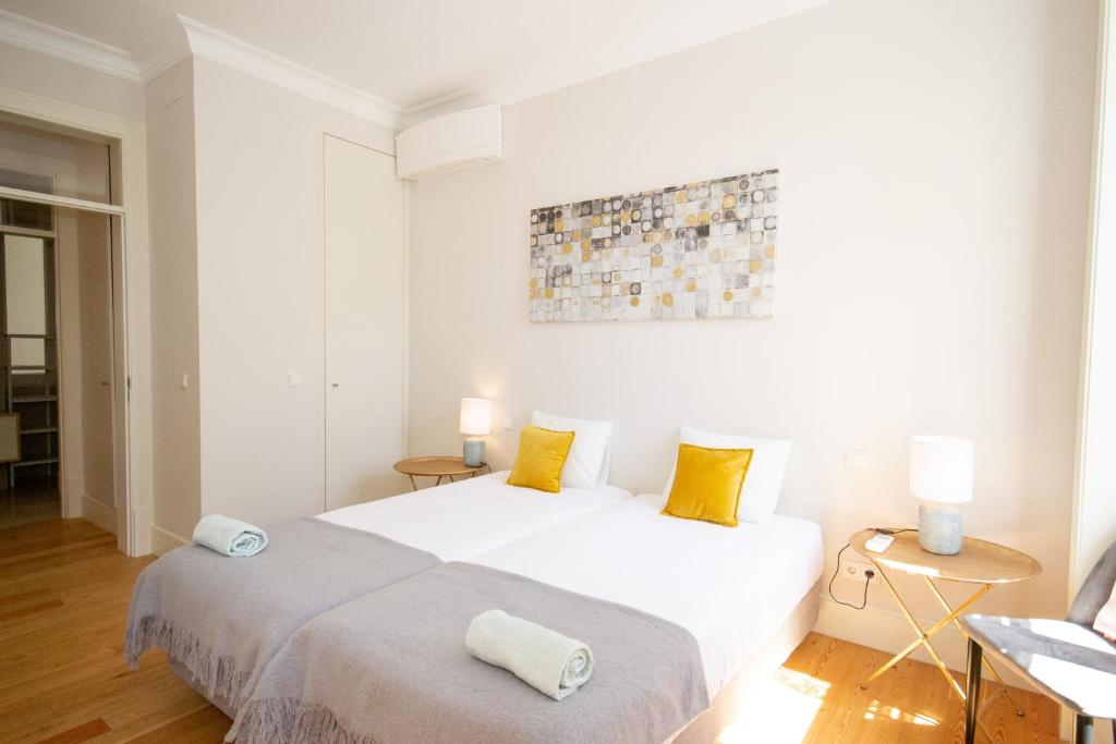 Bright bedroom with two single beds, white bedding, yellow pillows, bedside tables, and wall artwork.