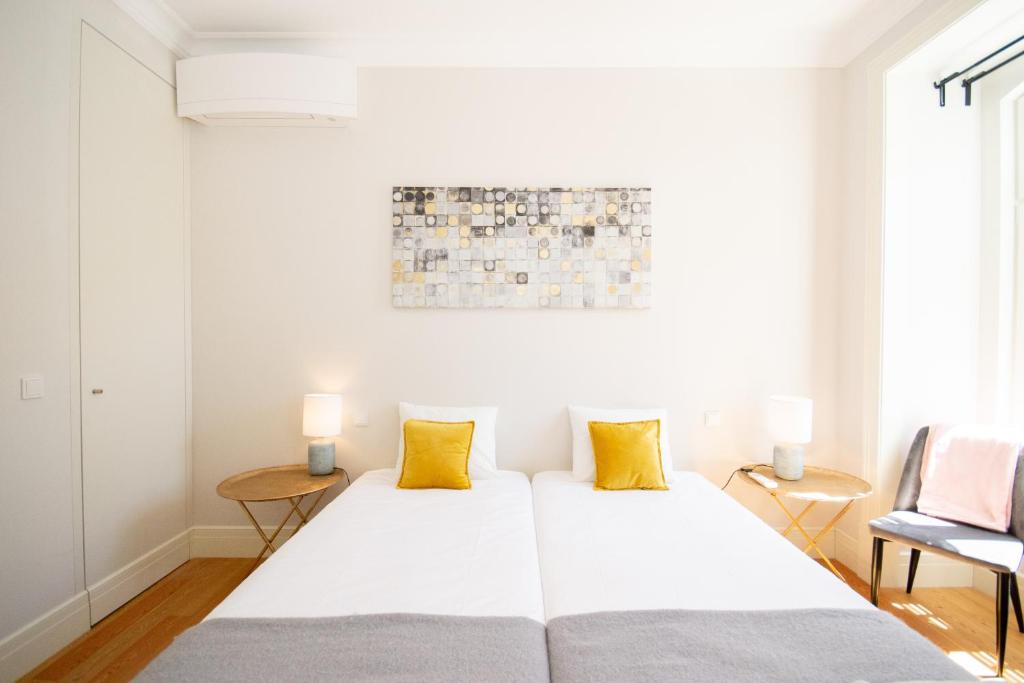 Minimalist bedroom with two single beds, yellow pillows, round wooden side tables, and wall art above.