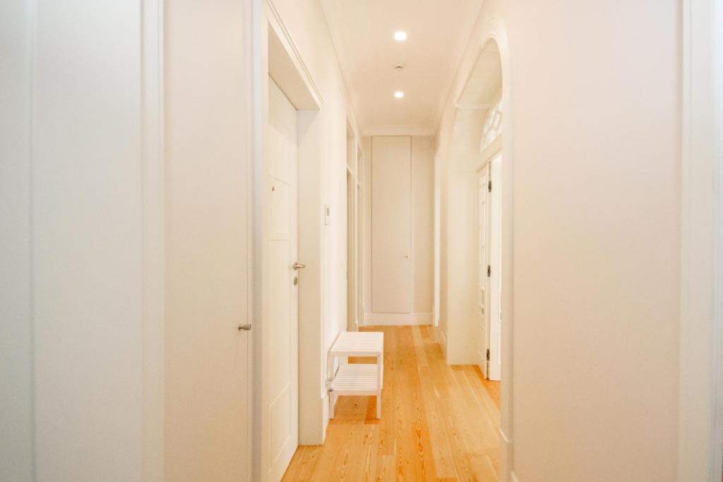 Bright hallway with light wood floor, white walls, white doors, and a small white bench.