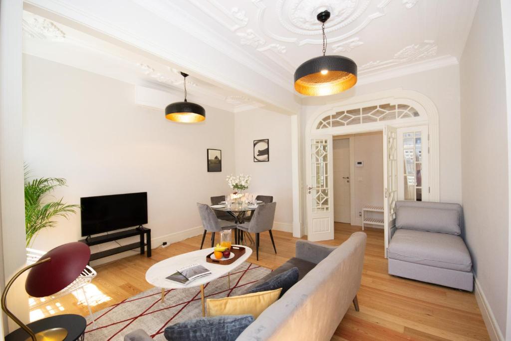 Bright living room with gray sofa, white coffee table, TV, dining table, and decorative ceiling lights.